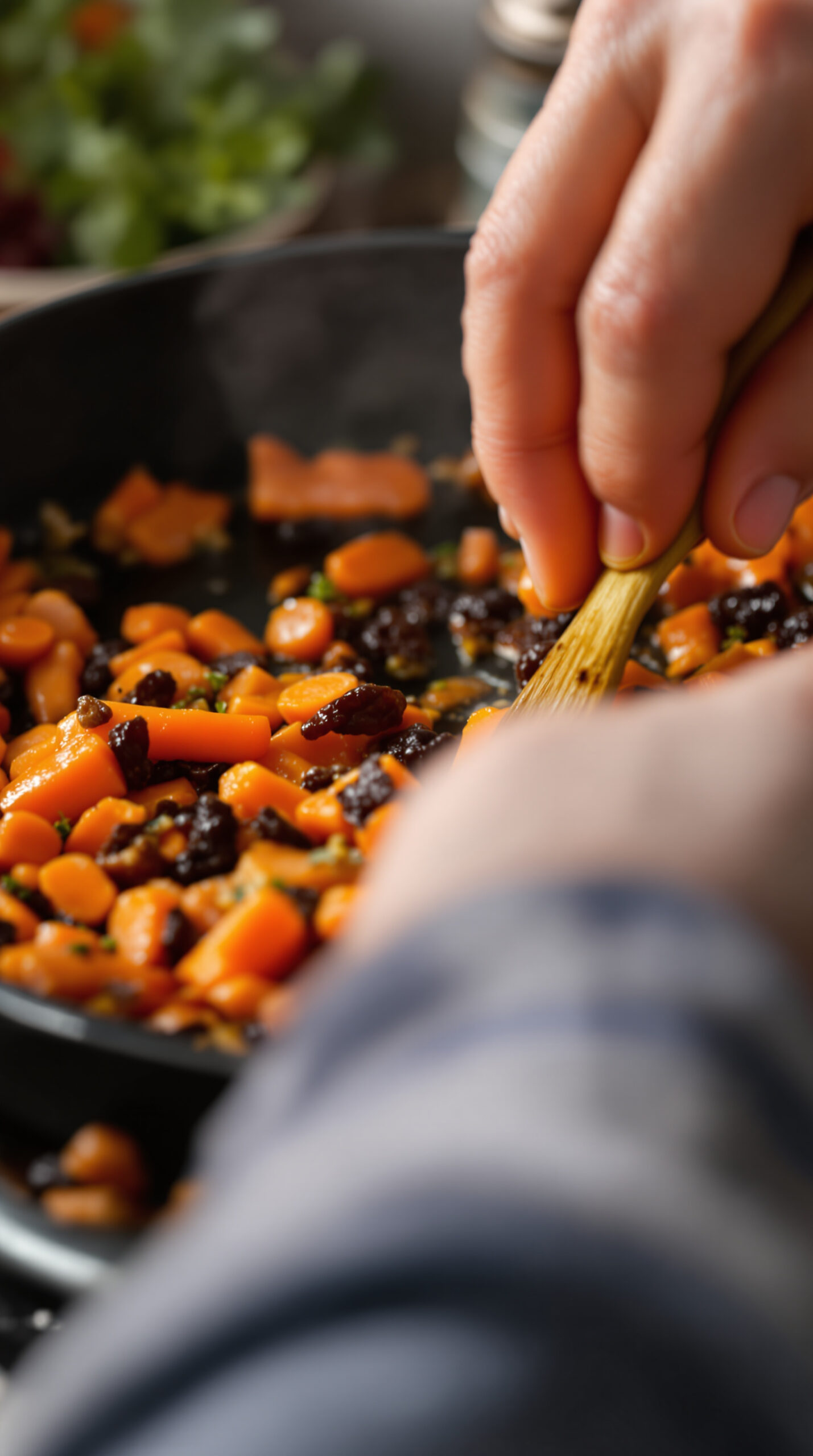 Main remuant des bâtonnets de carotte et des raisins secs caramélisant dans une poêle