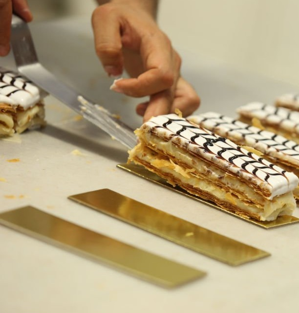 Mains étalant délicatement une crème pâtissière lisse sur une couche de pâte feuilletée dorée