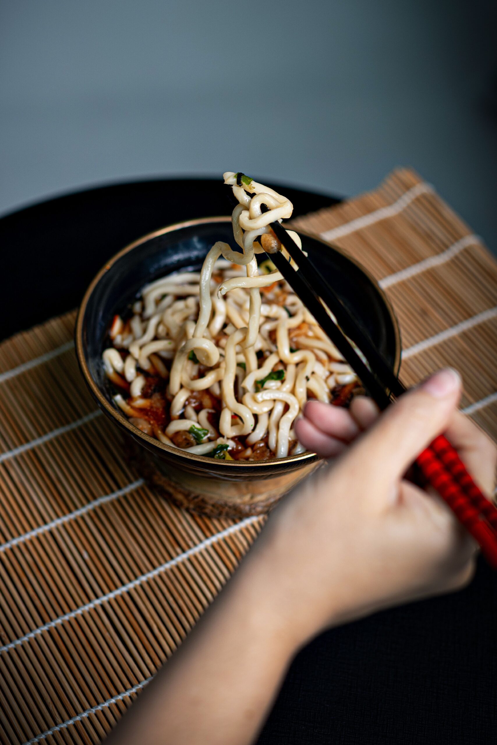 Main versant un bouillon dashi clair et fumant sur des nouilles udon dans un bol